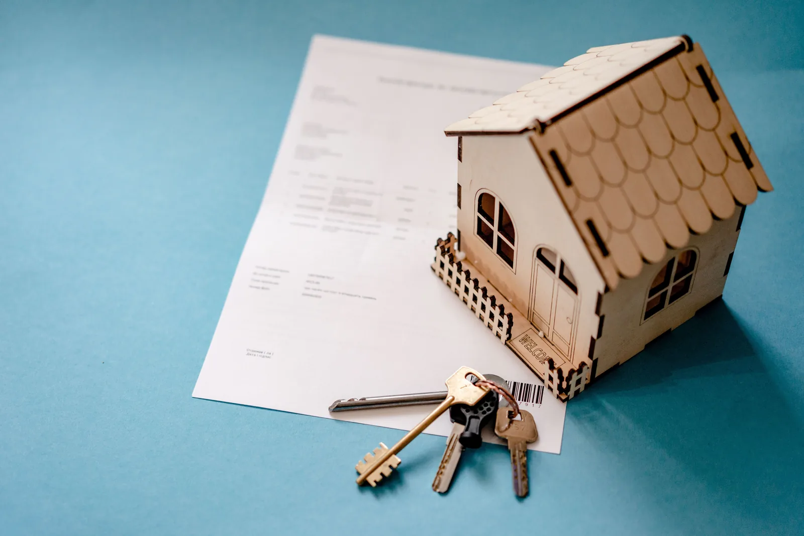 Wooden house model and keys beside a home purchase contract on a table